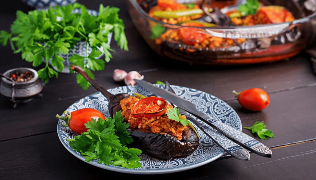 Ofengebackene Aubergine, gefüllt mit herzhafter Tomaten-Hackfleisch-Mischung, angerichtet mit frischer Petersilie und Cherry-Tomaten auf dekorativem Teller.