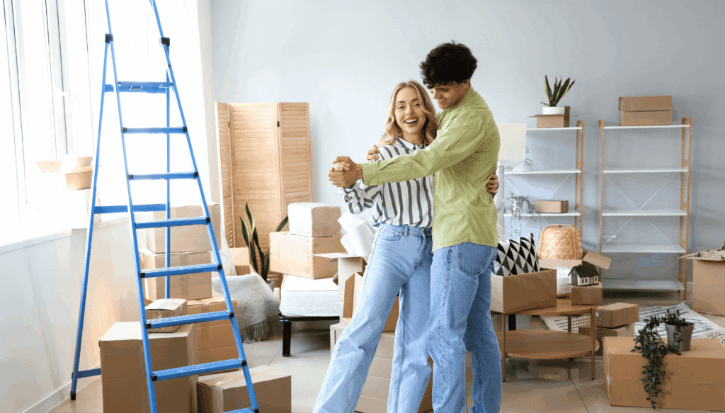 Frisch eingezogenes Paar tanzt inmitten von Umzugskartons in ihrer neuen Wohnung – Symbol für Freude beim Umzug und Start ins gemeinsame Zuhause.